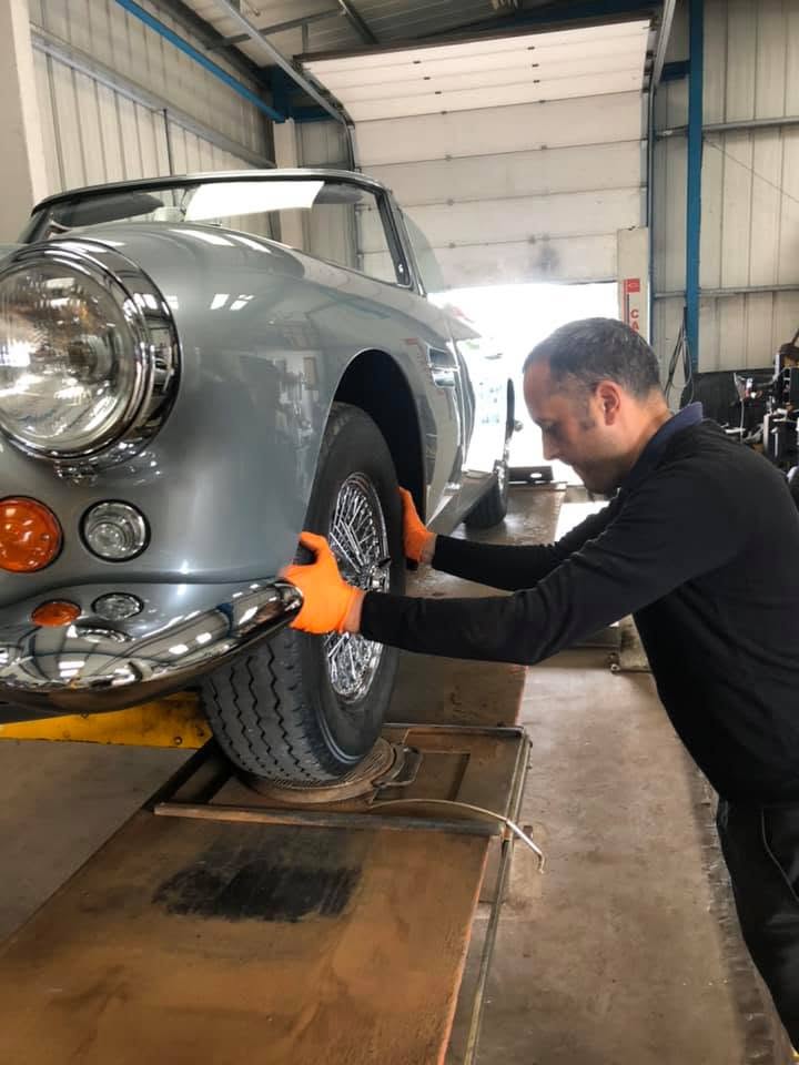 A Blossomgate Motors technician fitting a front wheel to a classic silver car on the ramp