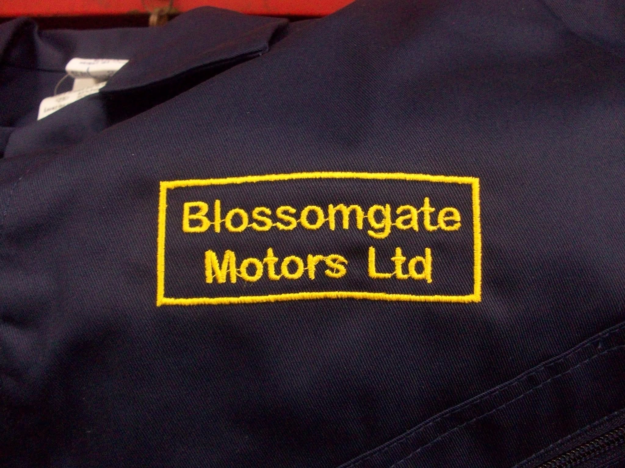 The yellow embroidered Blossomgate Motors Ltd badge on navy workwear