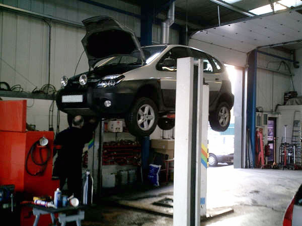 A car raised on a lift in the Blossomgate Motors workshop with a technician working underneath